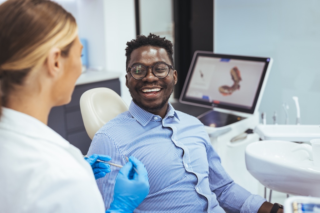 Smiling guy in dentist chair looking with trust at his doctor close up. Man Getting Teeth Treatment With Professional Stomatologist At Modern Clinic Closeup