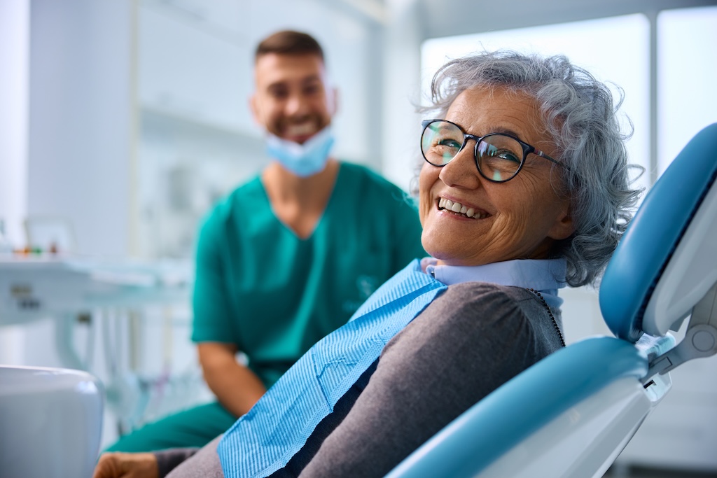 Satisfied senior woman at dentists office looking at camera after asking how long do dental crowns last for seniors - Prime Dental Satisfied senior woman at dentists office looking at camera after asking how long do dental crowns last for seniors